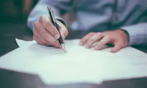 Dłoń pisze na papierze, być może notując, jak sprawdzić numer księgi wieczystej.