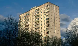 Blok mieszkalny z balkonami, otoczony drzewami. Może symbolizować służebność mieszkania, gdzie każdy balkon to osobna przestrzeń.