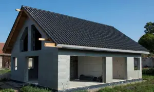 Budynek w stanie surowym otwartym, z dachem pokrytym czarną dachówką, bez okien i drzwi.