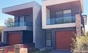 Nowoczesny dom szeregowy z drewnianymi drzwiami garażowymi i szklanymi balustradami na balkonach.