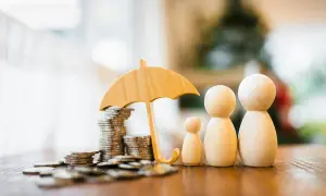 Drewniane figurki rodziny pod parasolem chroniącym stos monet. Symbolizuje to bezpieczeństwo finansowe i oszczędności, być może związane z opłatą skarbową.