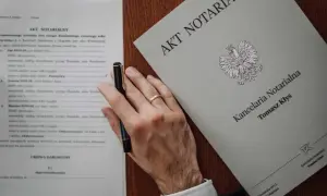 Akt poświadczenia dziedziczenia i umowa darowizny na biurku notariusza. Dłoń z obrączką trzyma długopis.