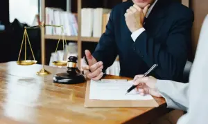 Prawnik omawia z klientem dokumenty, w tym pełnomocnictwo szczególne. Na biurku waga sprawiedliwości i młotek sędziowski.