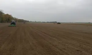 Traktory pracują na polu, przygotowując ziemię. Widać ślady po maszynach, które pomagają w obliczeniu hektara przeliczeniowego.