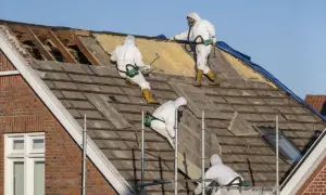 Pracownicy w kombinezonach usuwają stare pokrycie dachu, które może zawierać azbest. Co to jest azbest i dlaczego jest niebezpieczny?