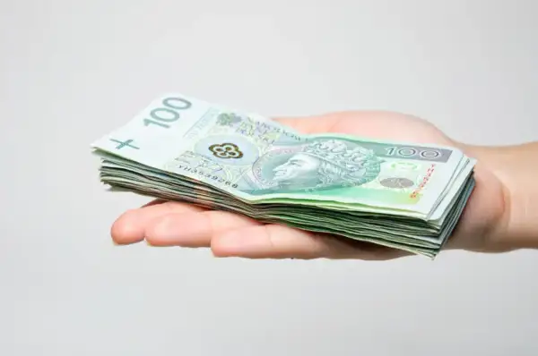 Dłoń trzyma stos banknotów 100 zł. To wstępny zstępny kapitał na nowy projekt.