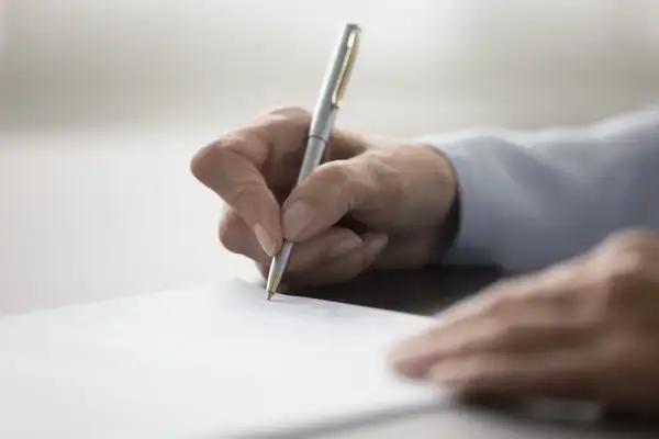 Dłoń pisze długopisem na dokumencie, finalizując umowę przyrzeczoną.