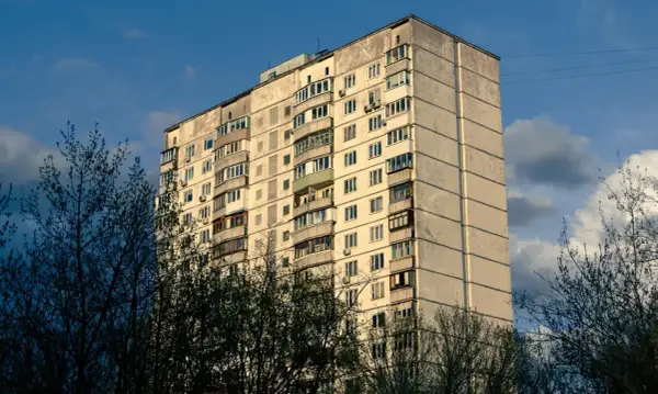 Blok mieszkalny z balkonami, otoczony drzewami. Może symbolizować służebność mieszkania, gdzie każdy balkon to osobna przestrzeń.