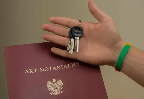 Dłoń trzyma klucze do nowego domu, obok leży akt notarialny. To symboliczny moment podpisania umowy przedwstępnej.