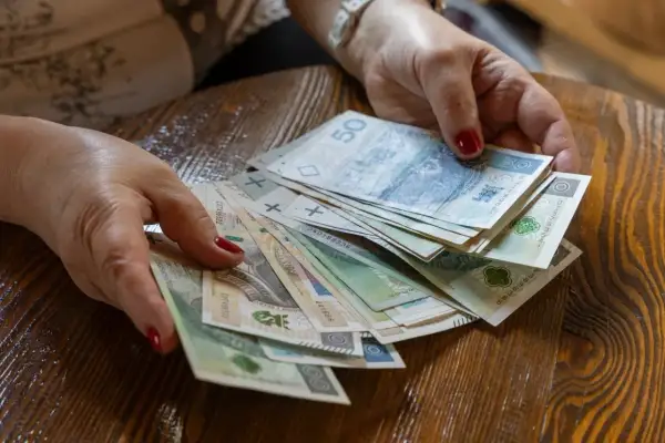 Dłonie z czerwonymi paznokciami trzymają stos polskich banknotów. Pytanie brzmi, ile razy można dać darowiznę dziecku.