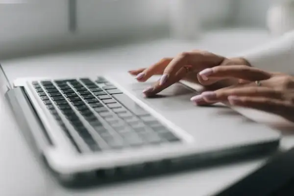 Dłonie z paznokciami malowanymi na jasny róż korzystają z touchpada laptopa.